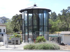 A glass enclosure with the conical glass lens inside is surrounded by chainlink fence.